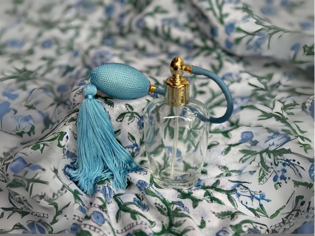 Perfume bottle with blue cap and tassel on a floral fabric background