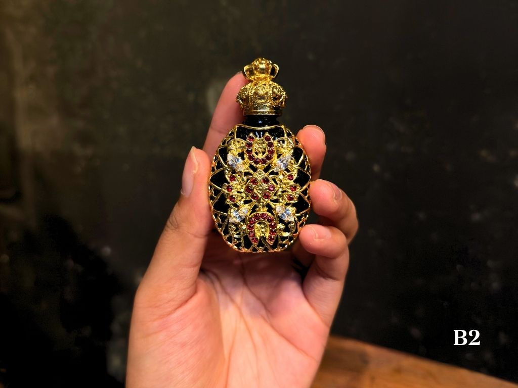Hand holding a decorative bottle with pink and silver gemstones against a dark background