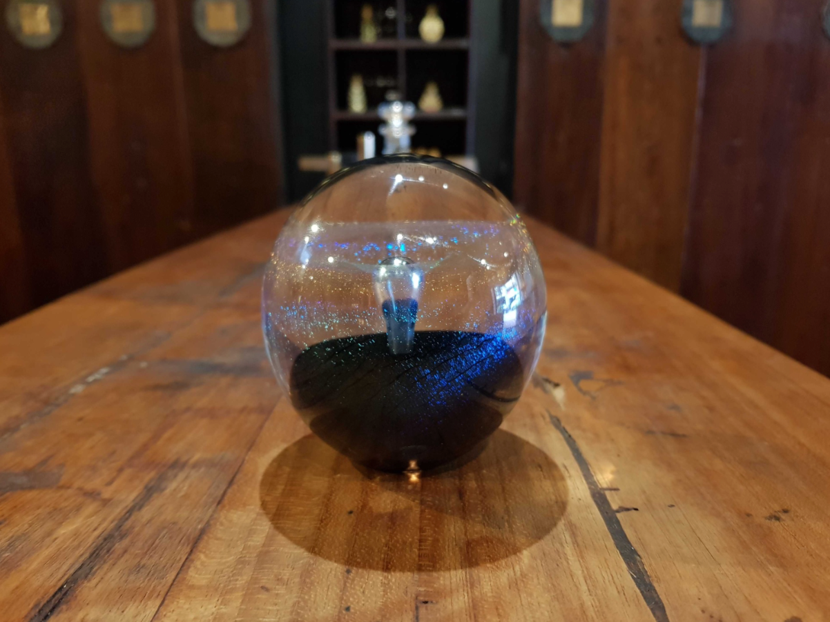 A spherical glass decorative object with a dark black base and glittery blue interior, sitting on a rustic wooden table in a warm, dimly lit room.
